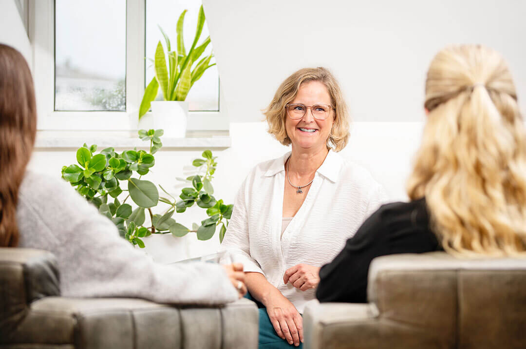 Kerstin Angermeier im Gespräch mit zwei Kundinnen. Sie trägt eine helle Bluse und lächelt ihre Kundin an.